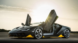Mörkgrå Lamborghini Centenario med uppfällda saxdörrar i motljus