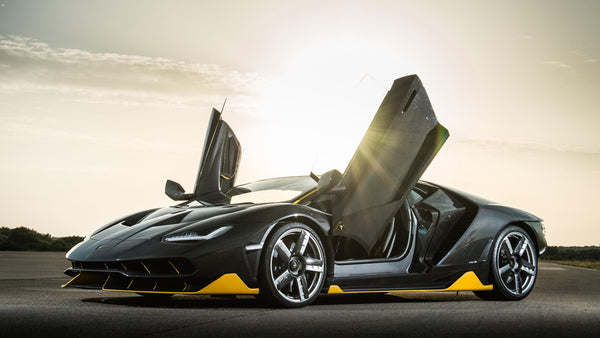Mörkgrå Lamborghini Centenario med uppfällda saxdörrar i motljus